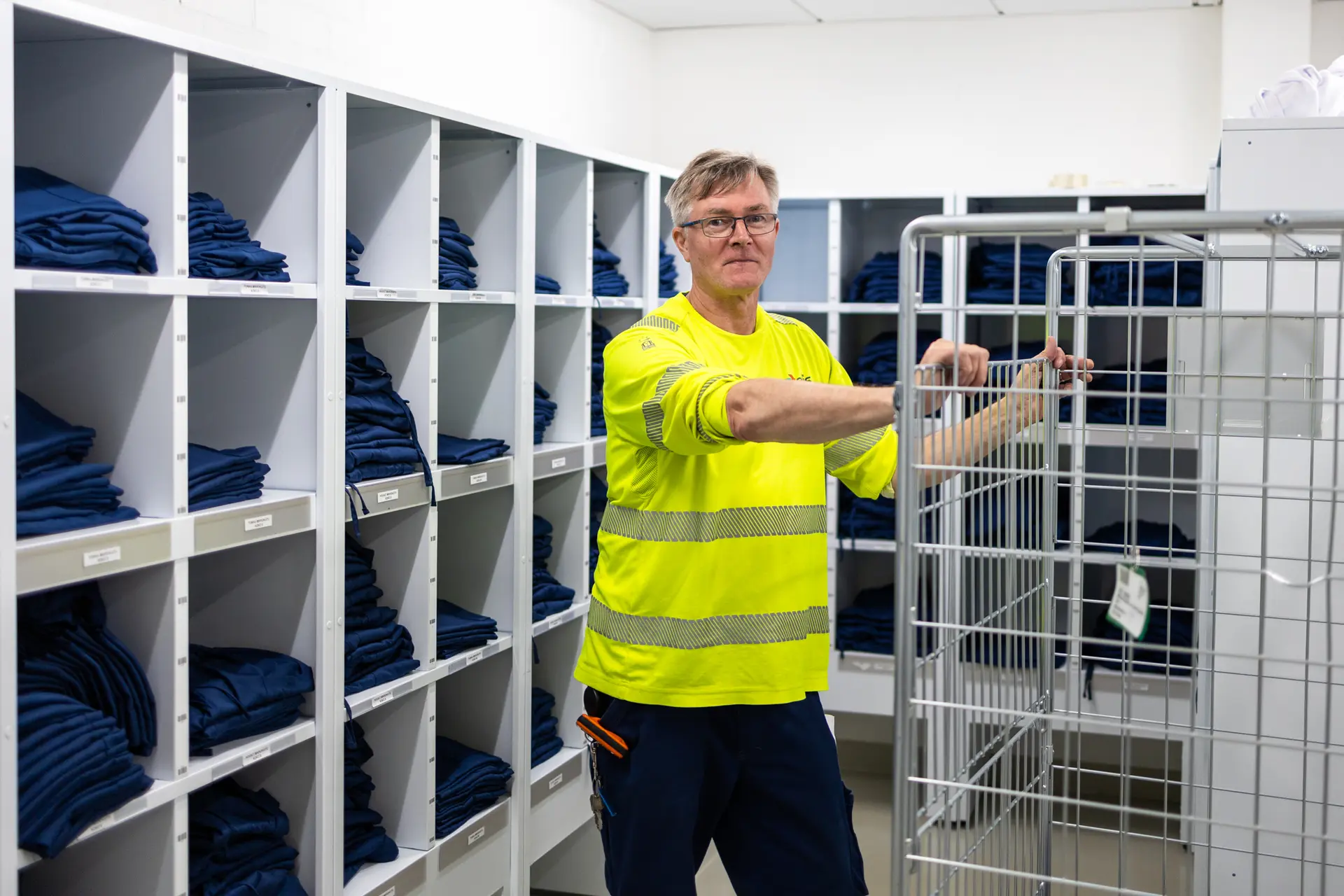 Mies nojaa tyhjään rullakkoon. Takana on iso hyllykkö täynnä sinisiä vaatteita.