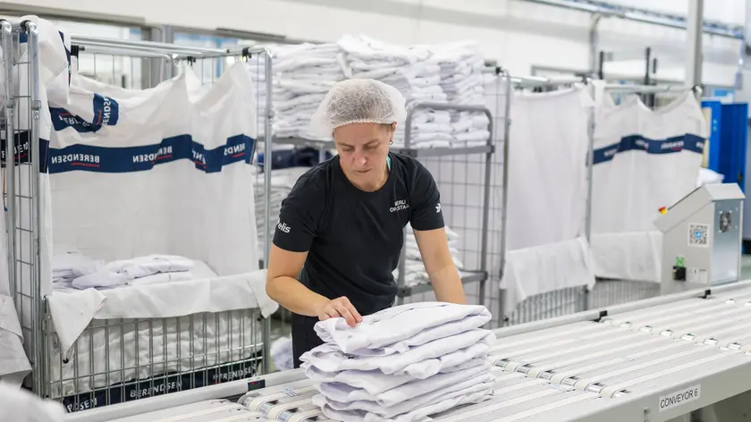 Nainen ottaa pinon viikattuja valkoisia paitoja liukuhihnalta syliinsä.