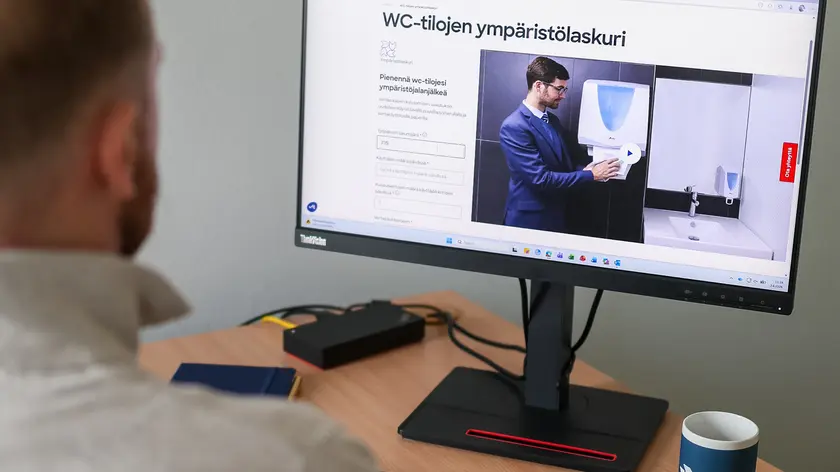 Tietokoneen ruudulla näkyy Elisin ympäristölaskuri. Työpöydän ääressä on mies.