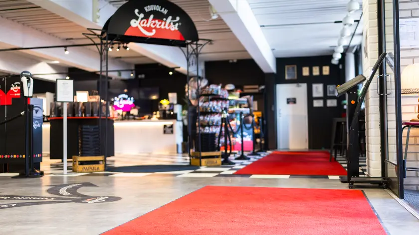 Kouvolan Lakritsin myymälän sisäänkäynti punaisella matolla, ruutulattialla ja näkyvällä Kouvolan Lakritsi -logolla.