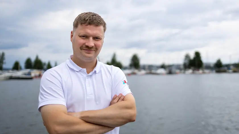 Henkilö valkoisessa pikeepaidassa seisoo kädet ristissä veden äärellä.