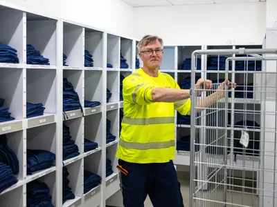 Mies nojaa tyhjään rullakkoon. Takana on iso hyllykkö täynnä sinisiä vaatteita.