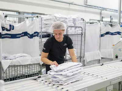 Nainen ottaa pinon viikattuja valkoisia paitoja liukuhihnalta syliinsä.