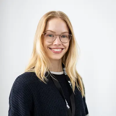 Hymyilevä nainen katsoo suoraan kameraan, valkoinen tausta.
